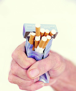 View of man's hand squeezing and crushing a pack of cigarettes