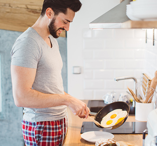 Man in sleeping clothes, about to put cooked eggs on a plate