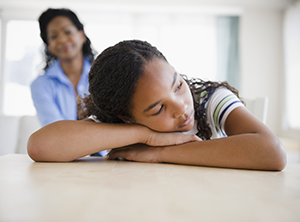 Teen with head on arms on table, with parent looking on