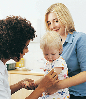 Woman holding baby on lap. Health care provider is preparing to give baby injection.