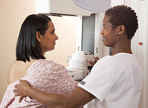 Woman standing next to mammography machine. Health care provider is positioning woman's breast on machine.
