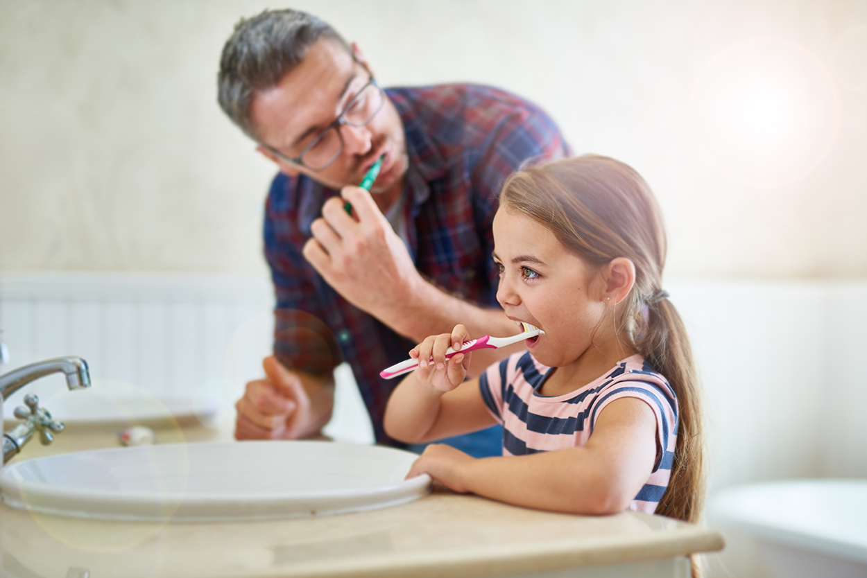 Father and daughter brushing their teeth in bathroom.